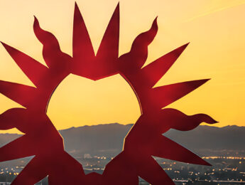 Abstract red sculpture resembling a Lion’s mane silhouetted against a golden sunset sky