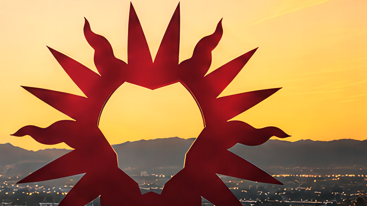 Abstract red sculpture resembling a Lion’s mane silhouetted against a golden sunset sky