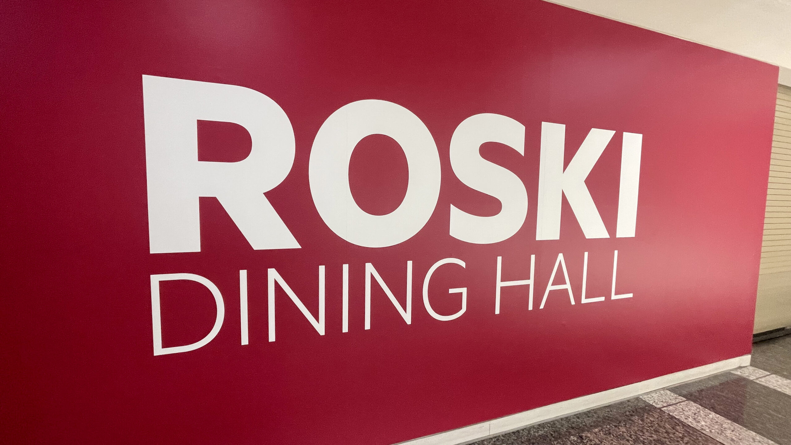 Close-up of a bright red wall featuring large white lettering that reads ROSKI DINING HALL