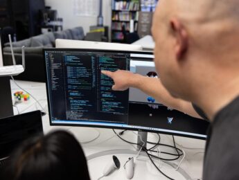 over the shoulder image of a professor and student looking at a monitor of code