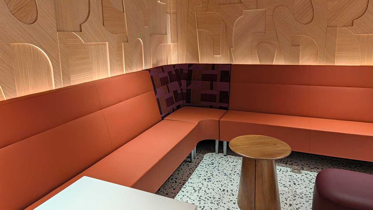 Modern lounge seating area featuring an L-shaped burnt-orange upholstered banquette surrounding a small round wood table.