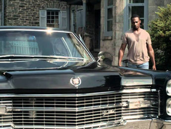 A man walking out of a large estate to a classic looking Cadillac