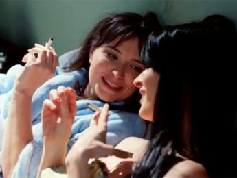 Movie scene with two women laughing while smoking cigarettes in bed