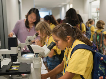Young girl looking into microscope at a STEM Summer session