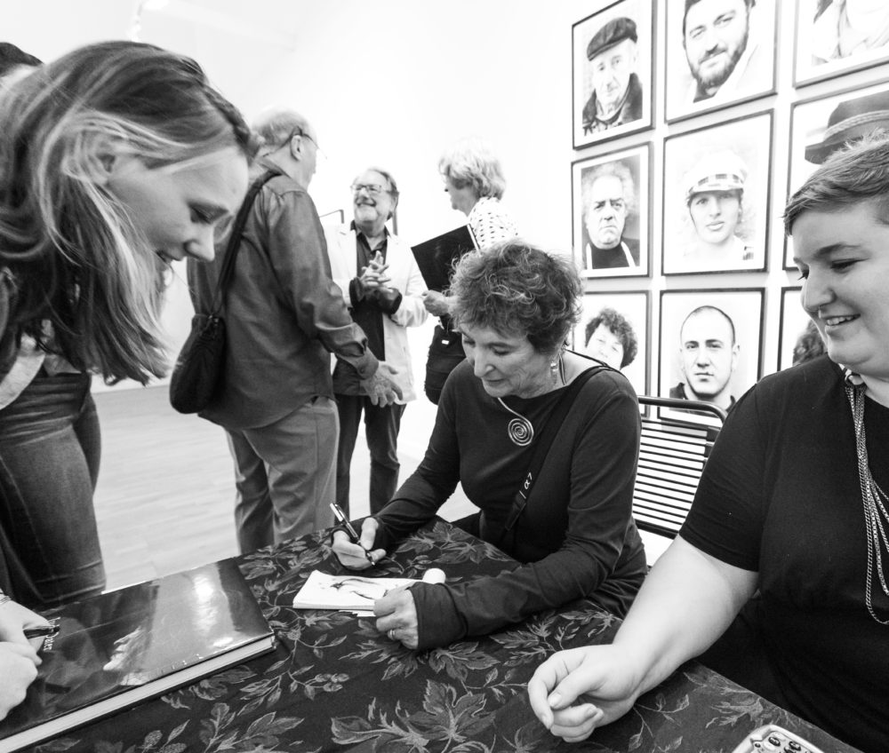 Black and white shot of Judy Dater signing autographs at "Only Human" exhibit