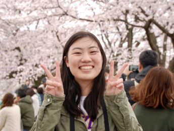 Veronica Rose Tan smiling and giving peace sign in front of cherry blossom trees