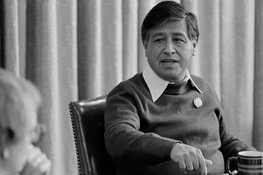 A black and white photo of Cesar Chavez meeting with others at a table seated.