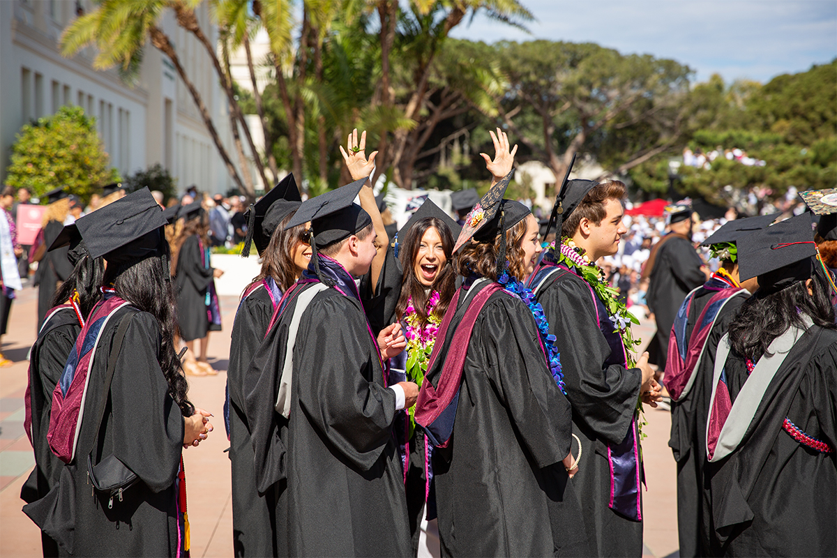 Undergraduate students enter LMU's commencement ceremony in caps and gowns cheering.