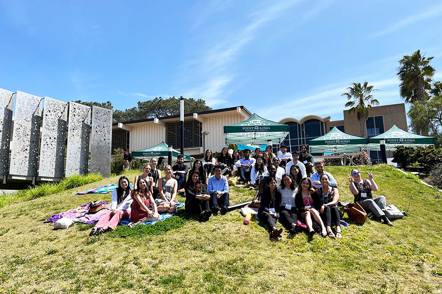 Group of Biology and Biochemistry Students and their faculty mentors sitting on a hill at the Coast Coast Biological Sciences Undergraduate Research Conference