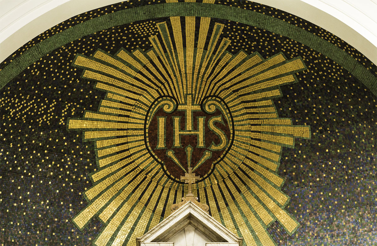The Jesuit emblem of the Holy Name of Jesus with three nails is rendered in mosaic above the High Altar of St. Aloysius in Glasgow. Photo by Lawrence OP