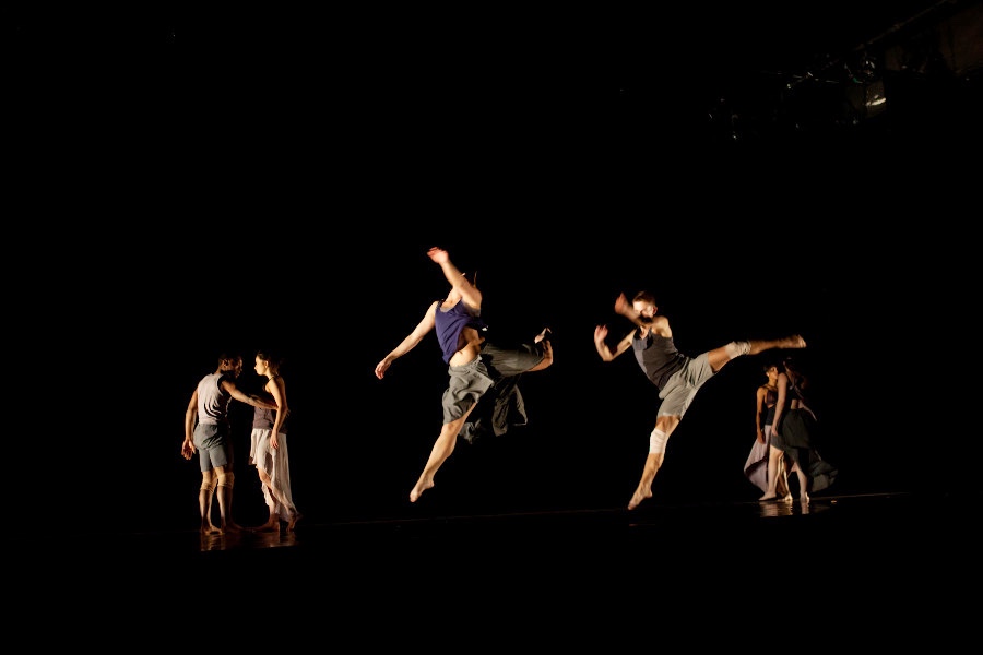 dancers leaping on stage against black backdrop