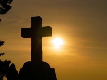 silhouette of cross with sun in background