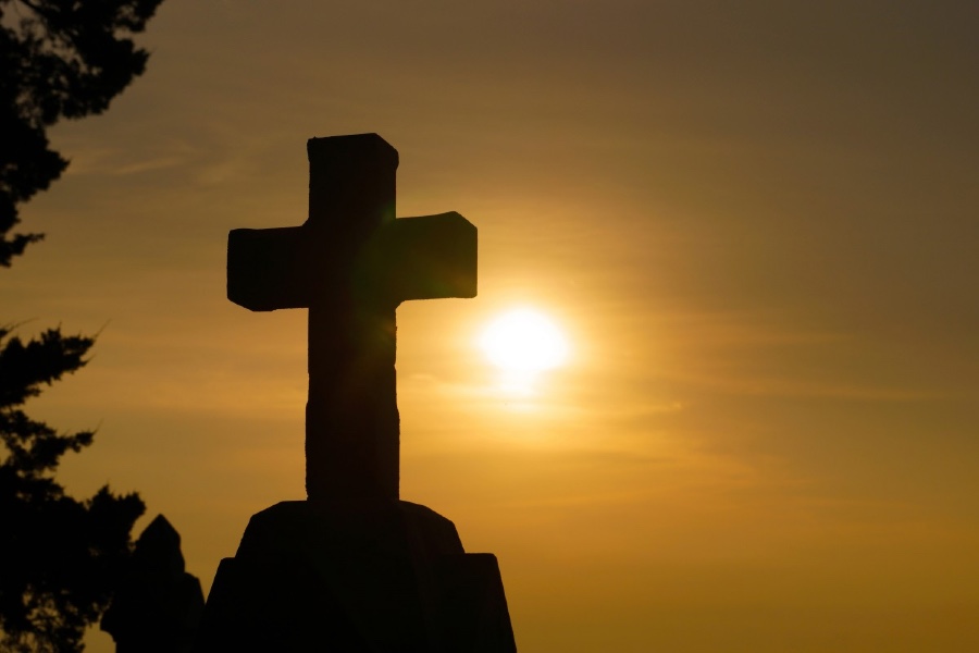 silhouette of cross with sun in background
