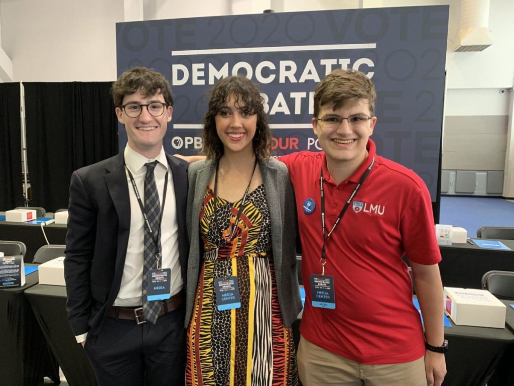 Students from The Loyolan pose in front of one of the Democratic Debate signs during the 2019 Democratic Debate at LMU.