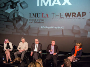 Five panelists speaking on a stage in front of a large IMAX branded screen