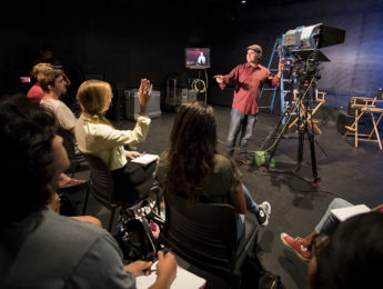 A professor explaining elements of a large video camera to a class in the black box