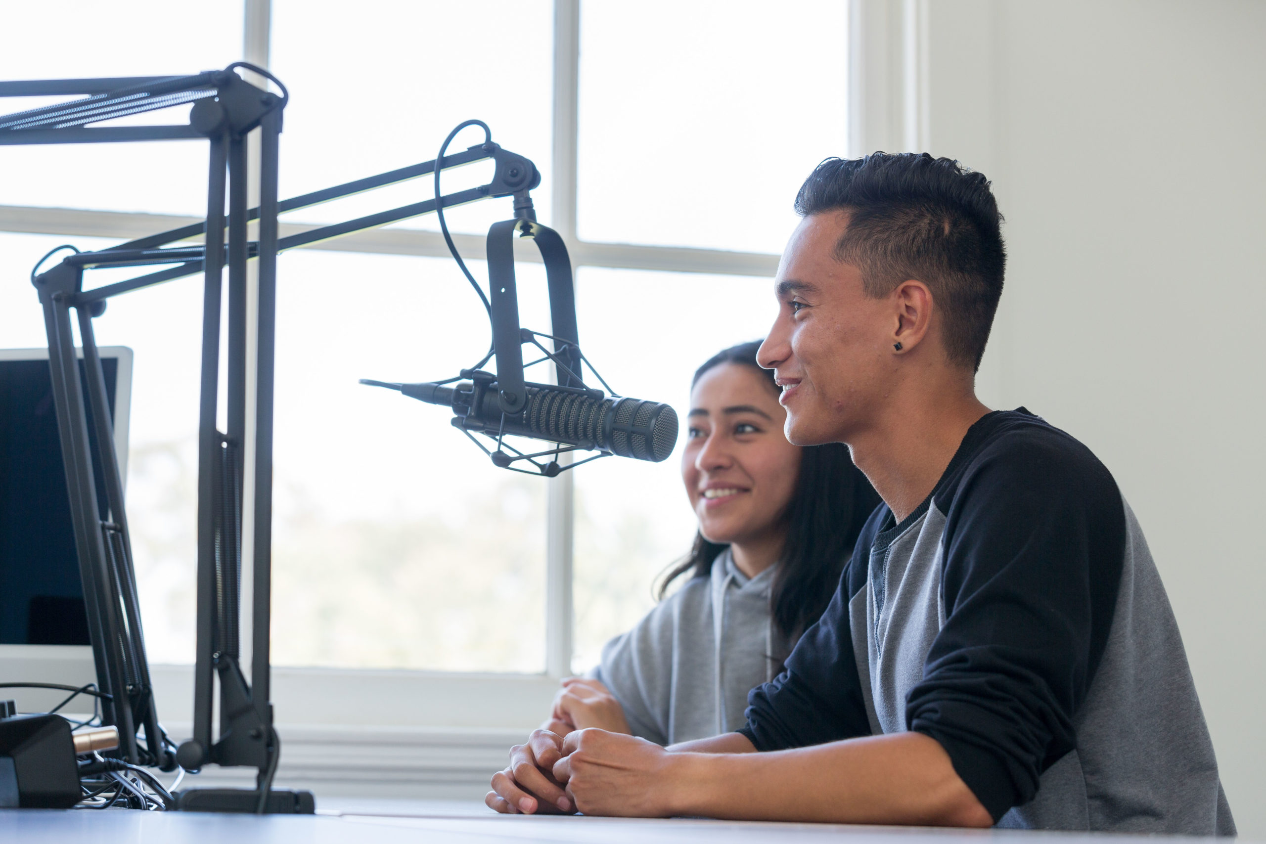 Two students sit inside a studio at a mic recording audio for a podcast.