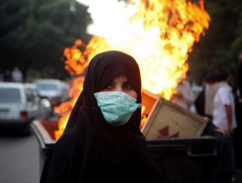 A woman protestor stands in front of burning pile while wearing a mask in Tehran, Iran