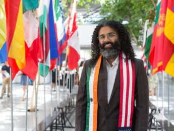 Krushan Naik stands in front of rows of international flags inside University Hall.