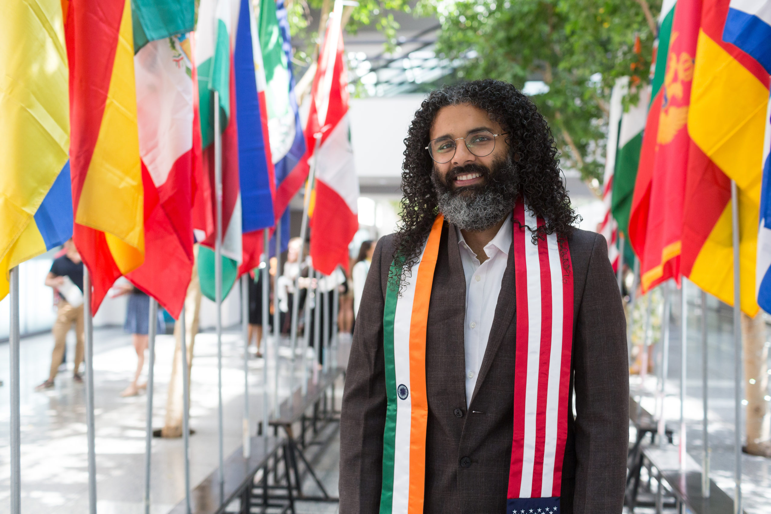 Krushan Naik stands in front of rows of international flags inside University Hall.