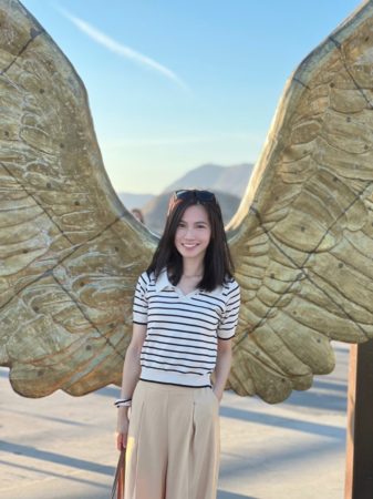A student stands outside in front of wood carved angel wings.