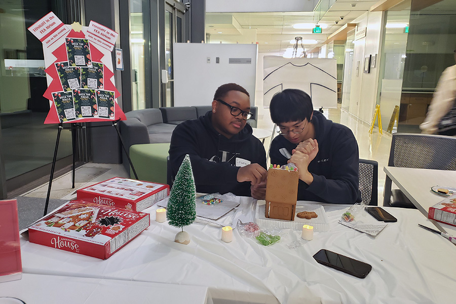 Two students of the HHSC society build and decorate a gingerbread house together.