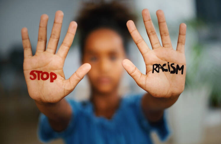 African american girl standing indoors and looking at the camera. She's showing an message that says Stop Racism on her hands.