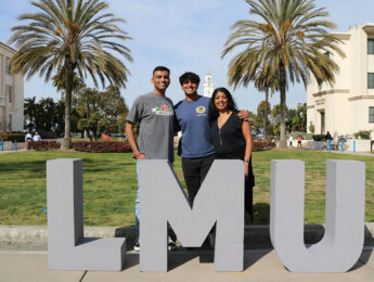 A student and their family members stand outside in front of grey letters: LMU.