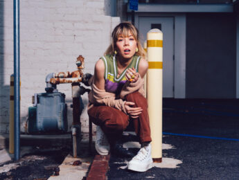 Jennette McCurdy poses in an industrial building with a brick wall.