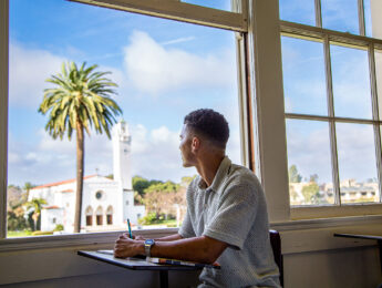 A student looking out a classroom window with Sacred Heart Chapel in the distance