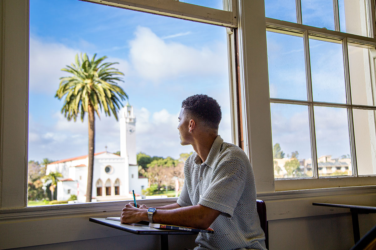 A student looking out a classroom window with Sacred Heart Chapel in the distance