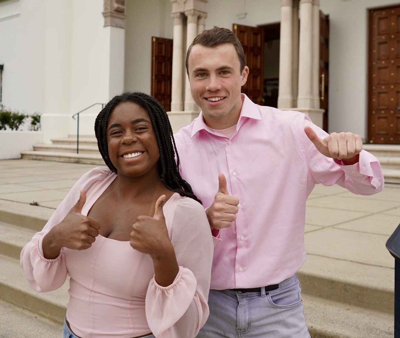 Two students in pink shirts and jeans stand on the chapel steps at LMU.