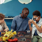 Portrait of young black boy building robots in engineering class with male teacher helping