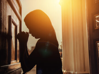 silhouette of woman kneeling and praying in modern church at sunset time