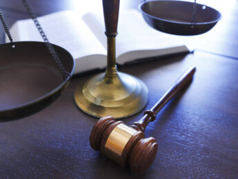 A gavel sits in front of a justice scale and an open law book.