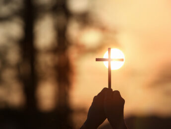 The yellow sunset sky and the bright sunlight background and the silhouette of a cross in hand