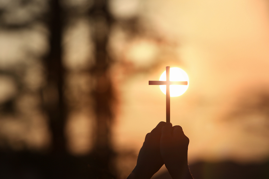 The yellow sunset sky and the bright sunlight background and the silhouette of a cross in hand