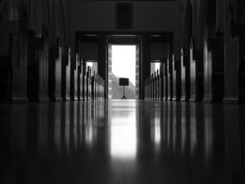 Black and white picture from inside an empty church looking toward the open exit door
