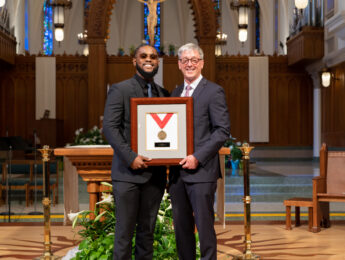 A student and the president stand holding an award inside the chapel during the annual student awards convocation.