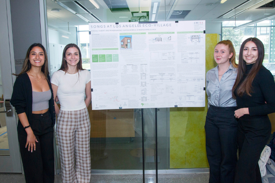 Four students smile standing next to the poster board for their project titled 'Songs at Los Angeles Eco-Village'