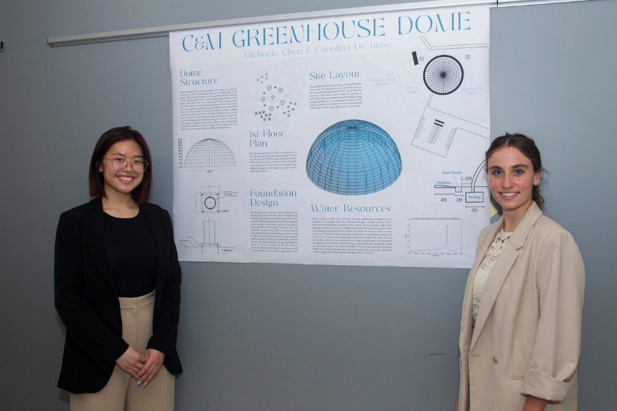 Two students smile standing next to the poster board for their project titled 'C & M Greenhouse Dome
