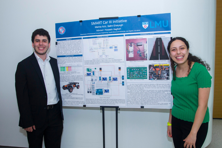 Two students smile standing next to the poster board for their project titled 'Smart Car III Initiative'