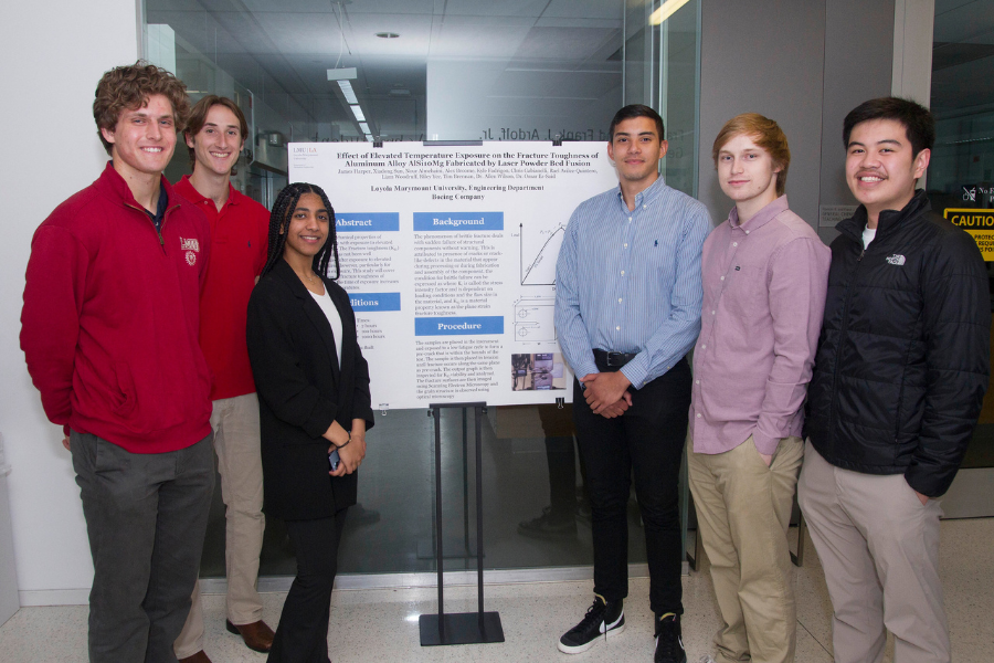 Seven students stand by the poster board for their project titled 'Effect of Elevated Temperature Exposure on the Fracture of Aluminum Alloy ALSioMg Fabricated by Laser Powder Bed Fusion
