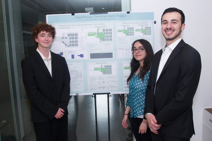 Three students smile, standing next to their poster board. The title of their project is 'Townhouse Development Project'