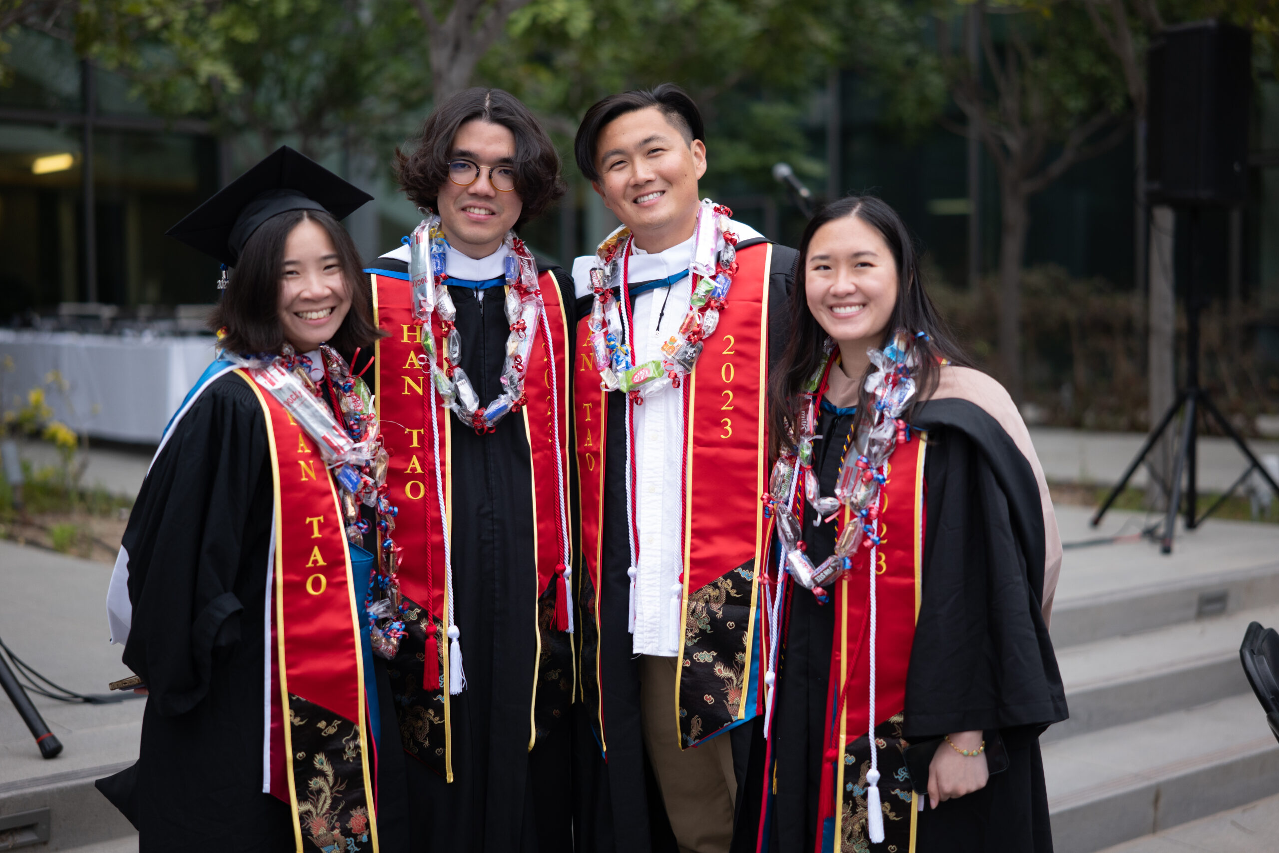 Students wearing regalia and Han Tao red stoles participate stand outside at API Graduation.