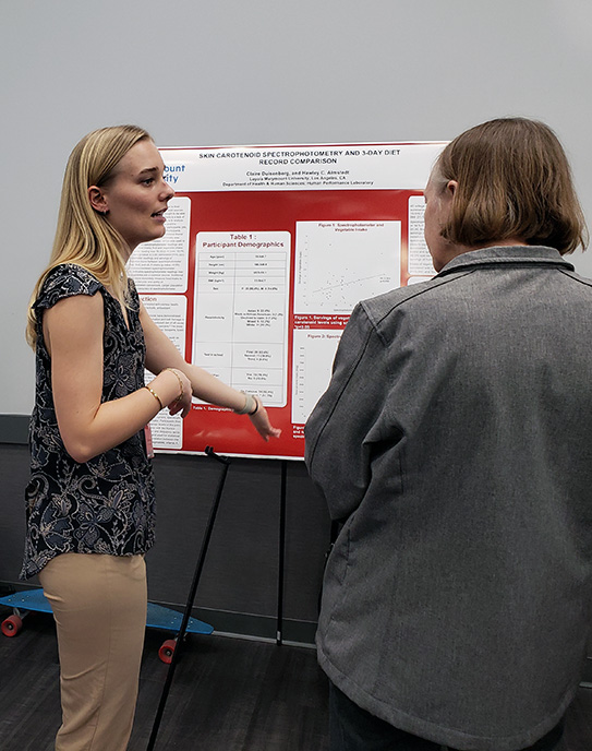 Student presents findings to individual at poster symposium
