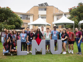 A crowd of students and administrators gather behind grey letters that spell LMU during move-in weekend.