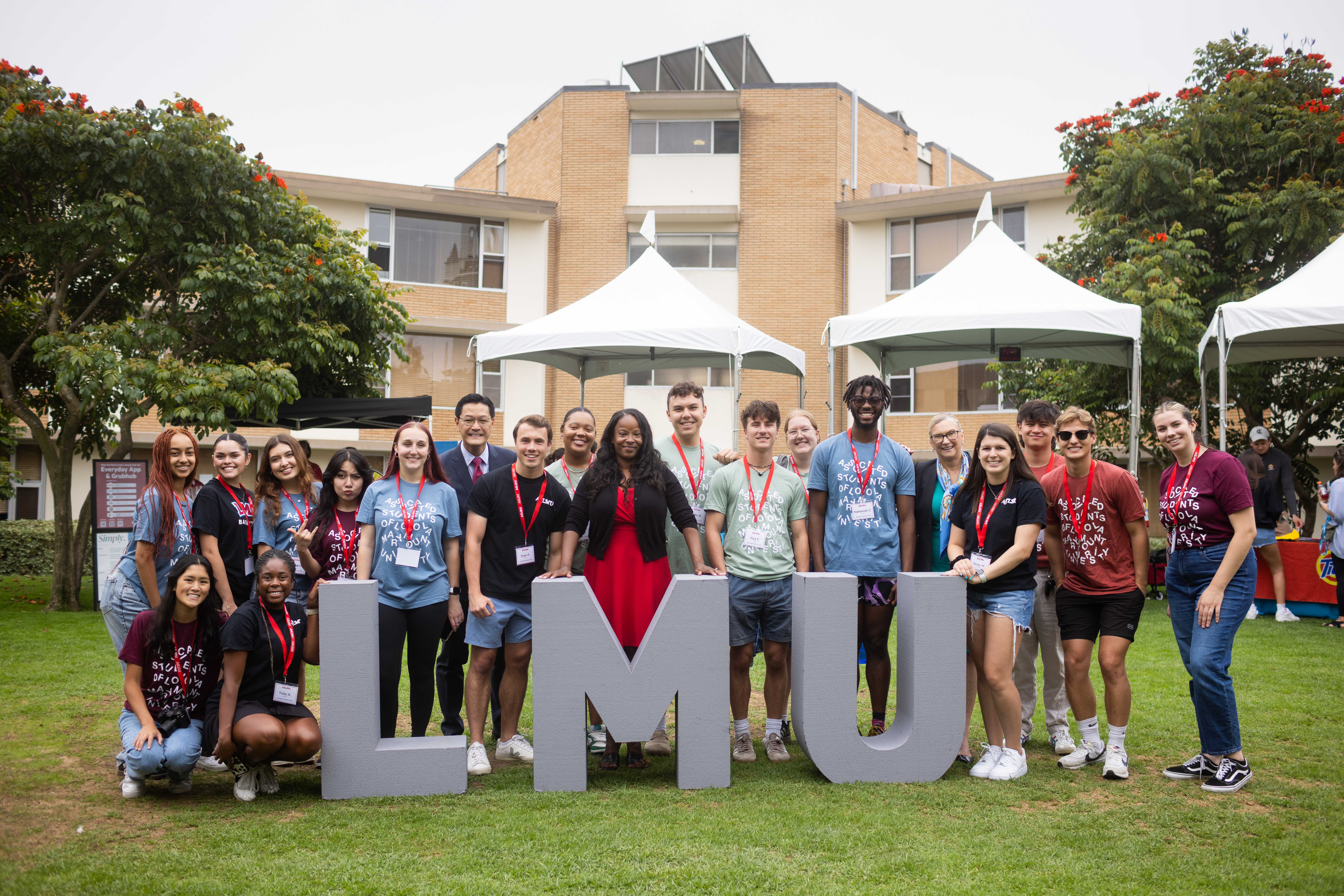 A crowd of students and administrators gather behind grey letters that spell LMU during move-in weekend.