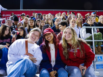 Students dressed in LMU gear sit in the stands during a men's soccer game.