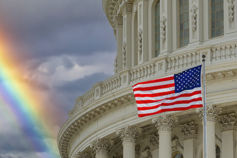 The Washington DC Capitol dome with waving American flag and rainbow sky background.
